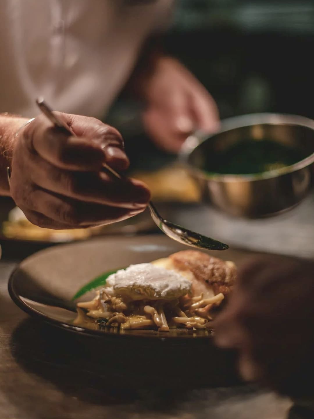 A chef adding the finishing touches to a plate of fish with a creamy sauce.