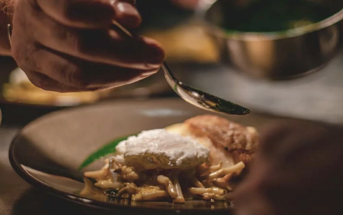 A chef adding the finishing touches to a plate of fish with a creamy sauce.