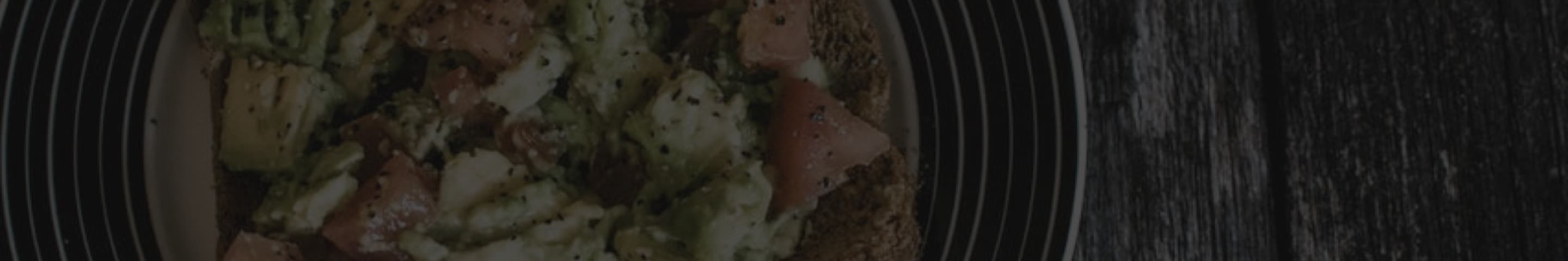 Plate with avocado and tomato on toast, sprinkled with black pepper, on a wooden table background.