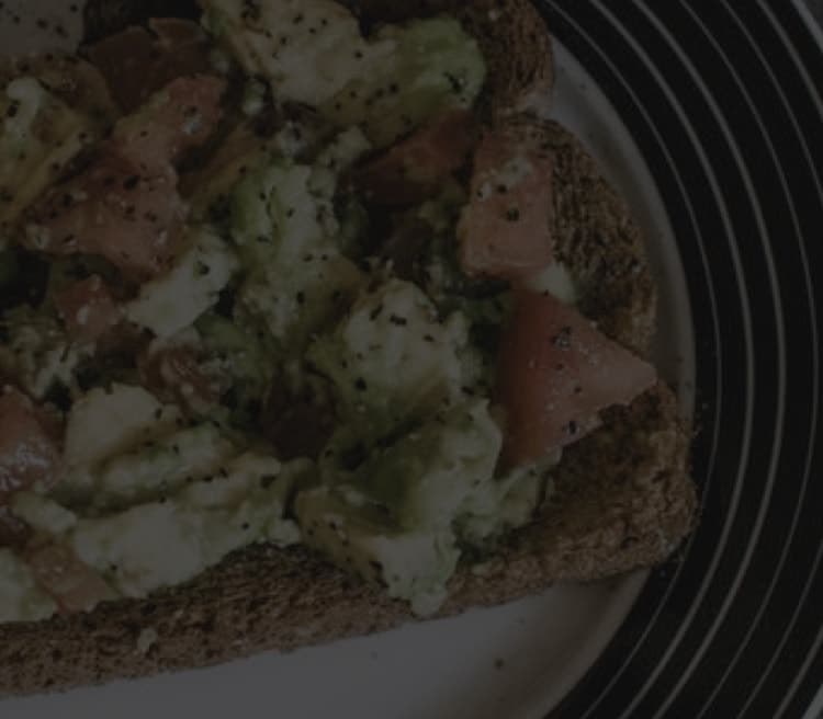 Plate with avocado and tomato on toast, sprinkled with black pepper, on a wooden table background.