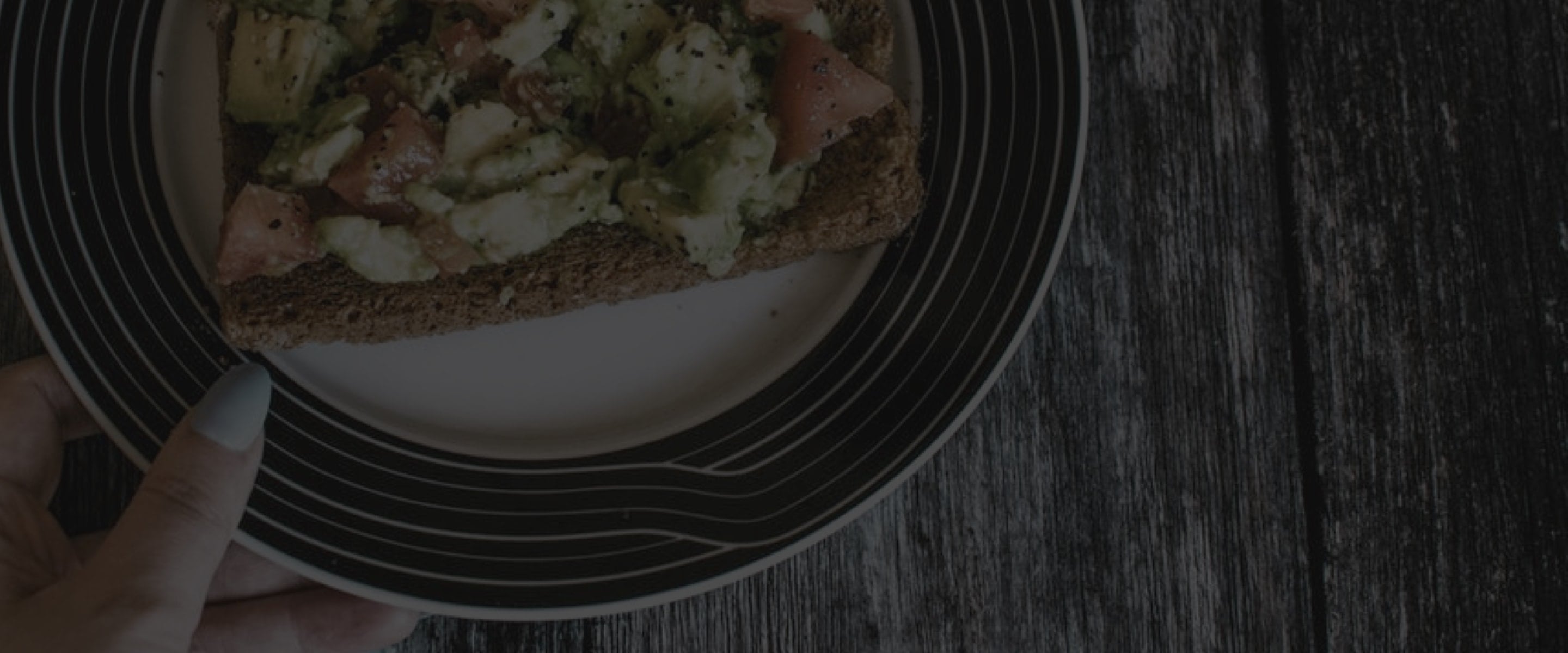 Plate with avocado and tomato on toast, sprinkled with black pepper, on a wooden table background.
