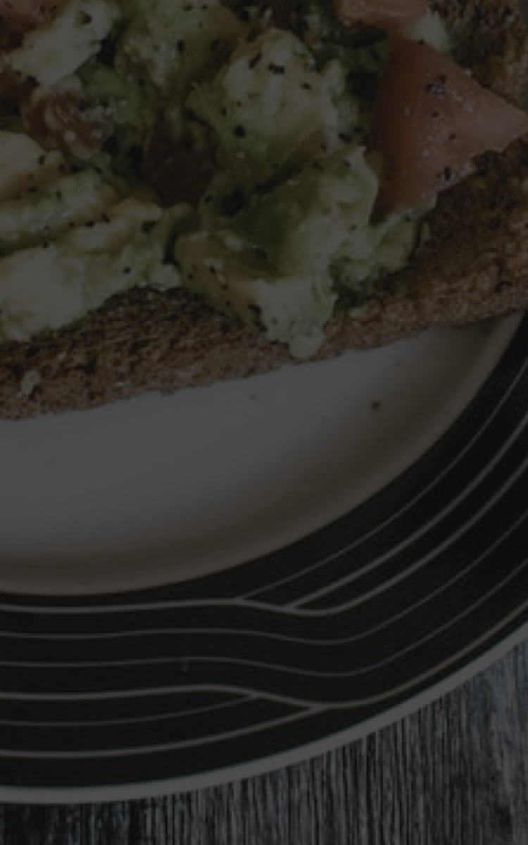 Plate with avocado and tomato on toast, sprinkled with black pepper, on a wooden table background.