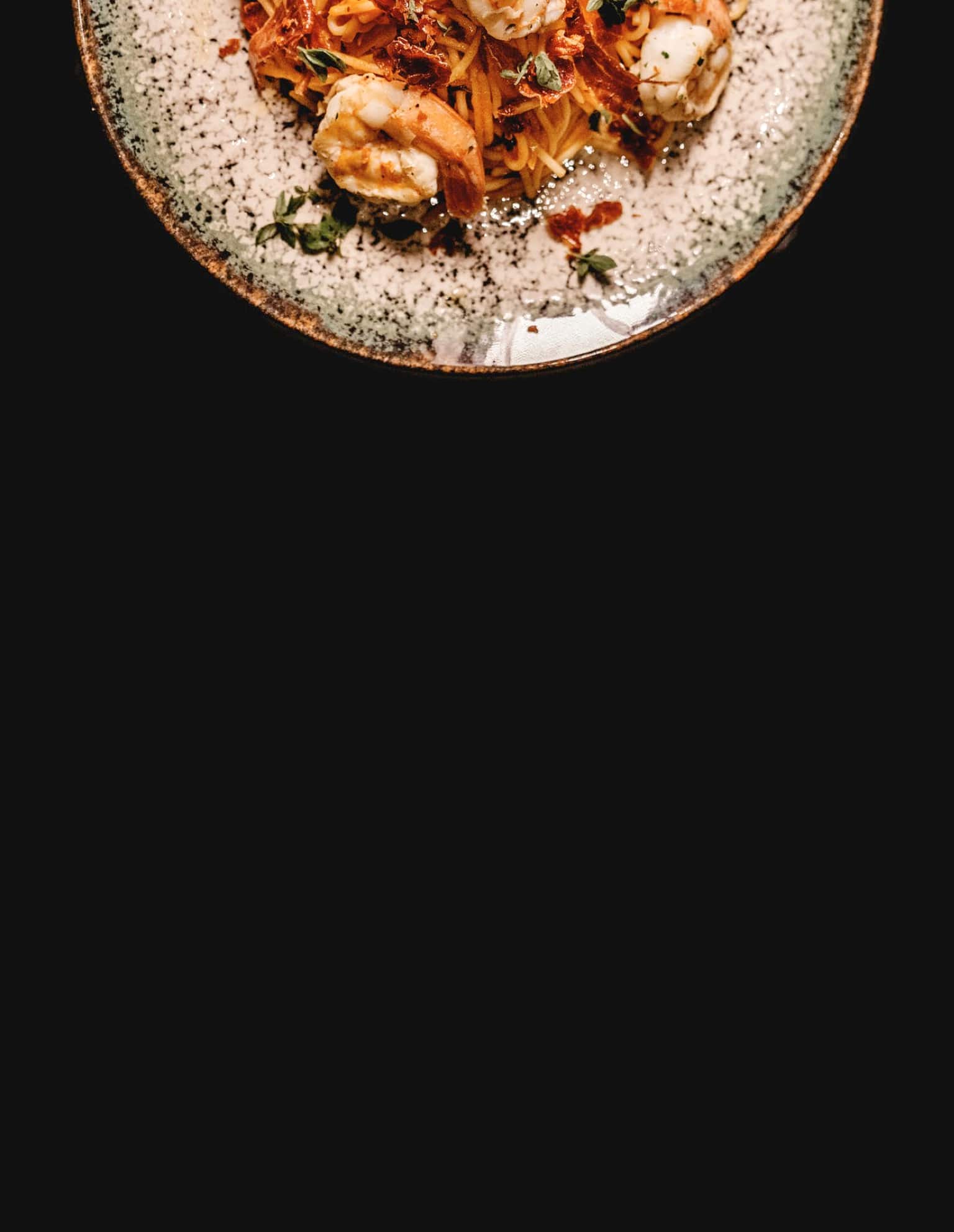 A plate of spaghetti with shrimp, marinara sauce and herbs.
